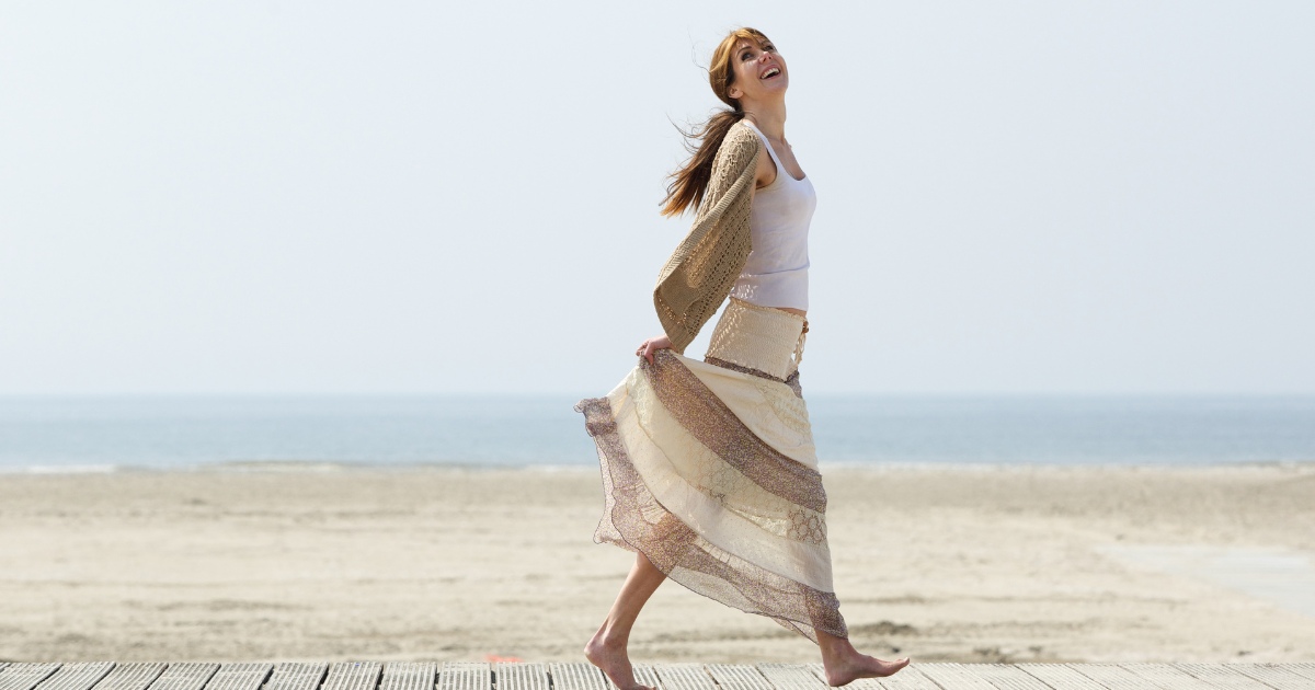 A joyful, mild-aged woman standing and dancing on the beach.