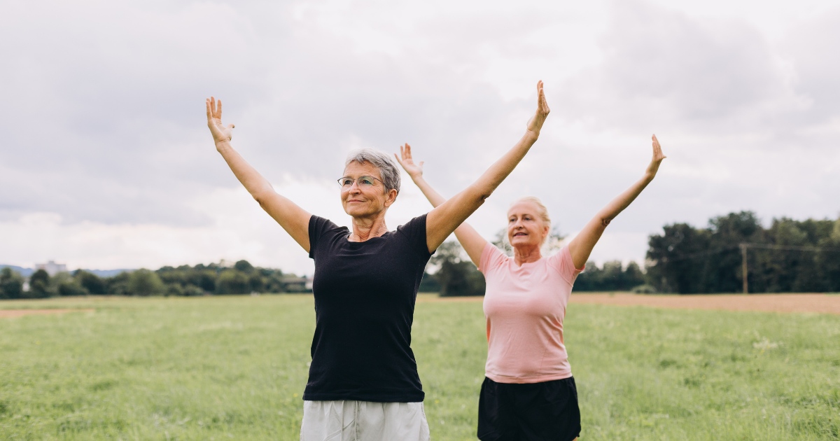 Two older women exercising outdoors in a grassy field.